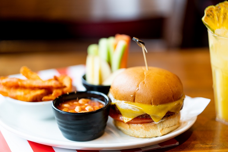 A small cheeseburger and a pot of beans on a plate