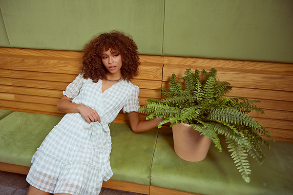 Woman in Quiz dress sat on a bench next to a plant